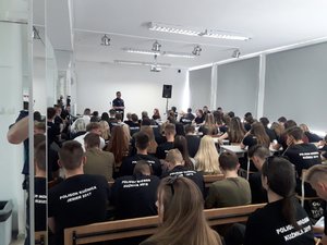 policjant z drogówki rozmawia z młodzieżą siedzącą w szkolnych ławkach