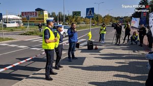 Grupa osób stoi przy drodze. Są to uczestnicy akcji, a lewej strony stoją policjanci.