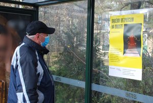 Zdjęcie kolorowe. Teren przystanku autobusowego. Mężczyzna ogląda plakat