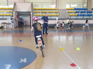 Zdjęcie kolorowe. Szkolna hala sportowa, na terenie której dzieci zdają egzamin na kartę rowerową pod okiem policjanta