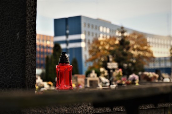 zdjęcie przedstawia zbliżenie na znicz leżący na pomniku. W tle budynek Komendy Wojewódzkiej Policji w Katowicach